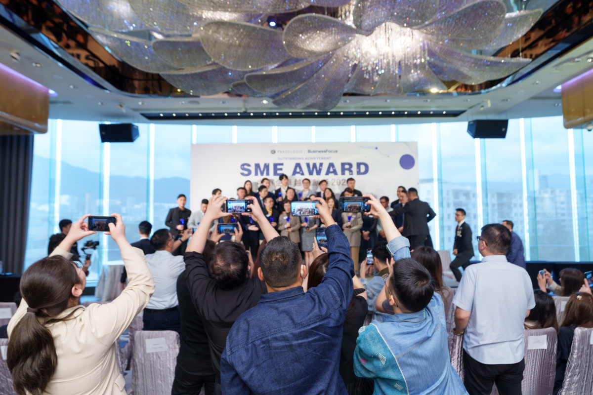 香港 BusinessFocus 中小企卓越成就獎 2025 頒獎典禮現場,觀眾舉手機拍攝舞台上得獎團隊與「SME AWARD」背板合影